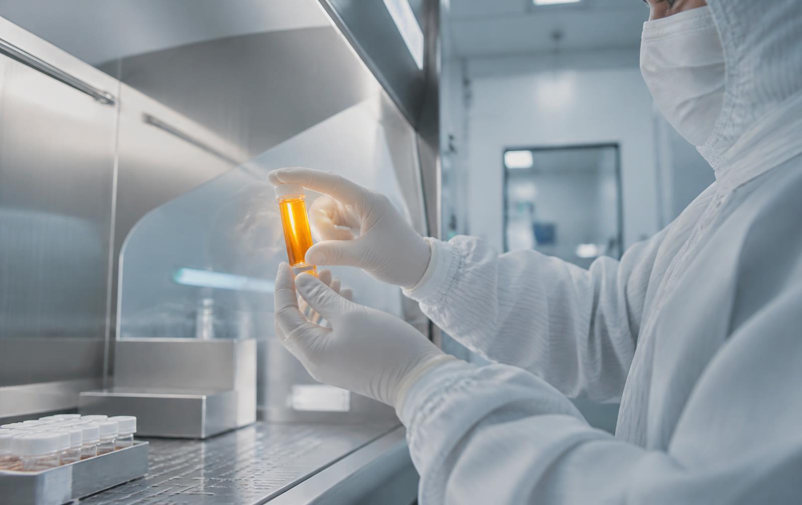 A scientist in a GMP cleanroom holding a vial of amber adipose-derived stem cell suspension
