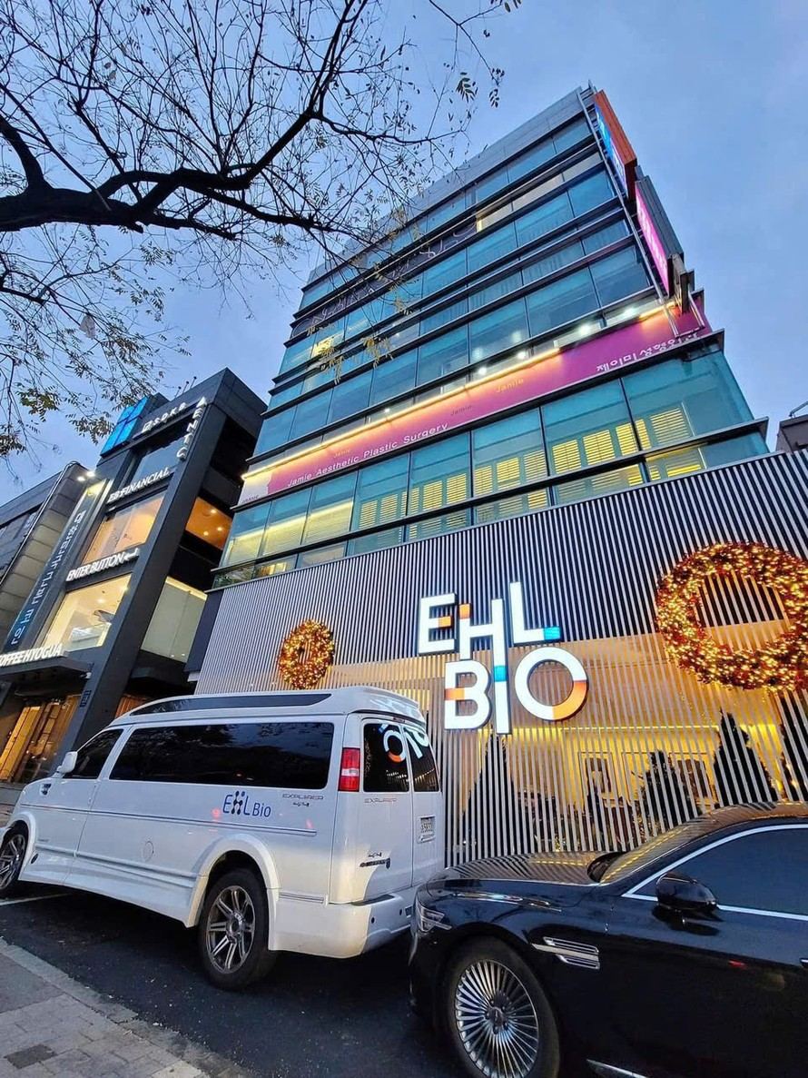 Glass-fronted EHL Bio Cell Center building in Gangnam, Seoul at dusk, with the illuminated EHL BIO sign at street level and the hospital's patient shuttle van parked outside